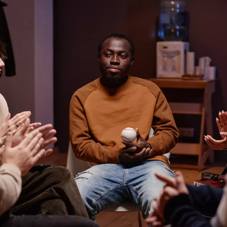 Horizontal shot of psychologist and clients clapping hands to young man after getting acquainted to him