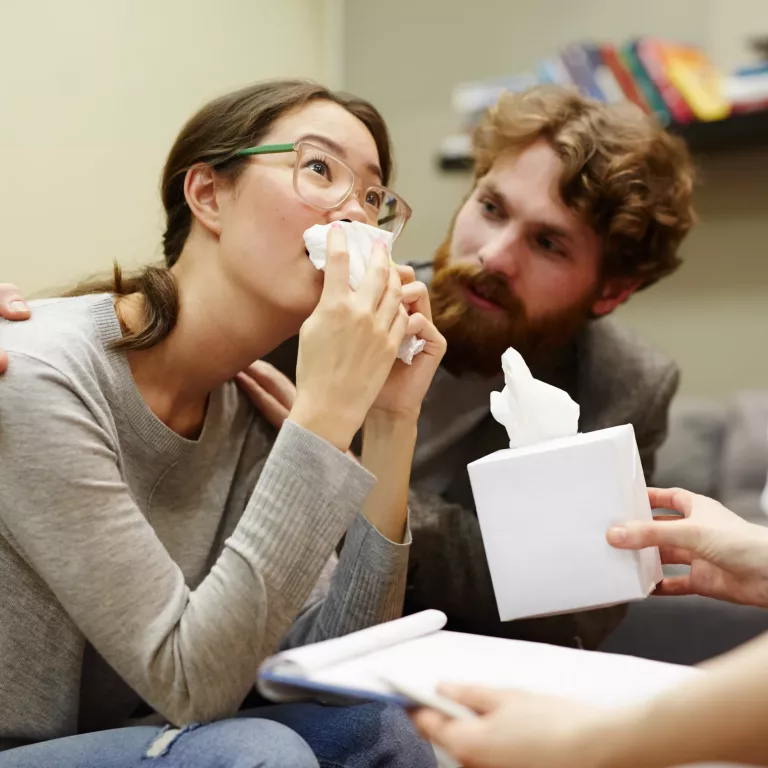 Crying woman with handkerchief looking at counselor while young man supporting her